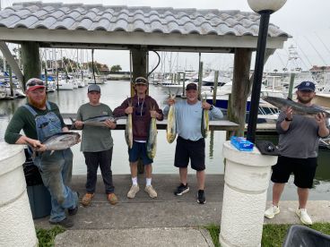 A group of anglers proudly displaying their catch, including Mahi Mahi and Tuna, at a marina after a successful fishing trip.