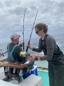 Two anglers engaged in fishing action on a boat, with one preparing to reel in while the other assists, showcasing a dynamic fishing experience.