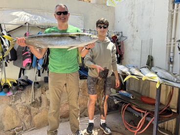 Two anglers proudly displaying their catch, including a large Yellowtail and a Grouper, at a fishing facility.