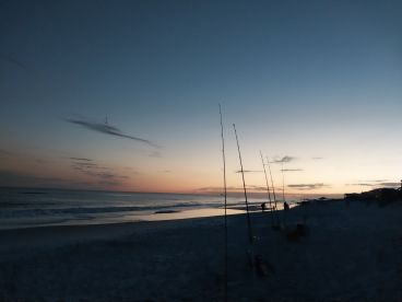 A serene beach scene at dusk with fishing rods set up along the shoreline, capturing the tranquil atmosphere of a fishing outing.