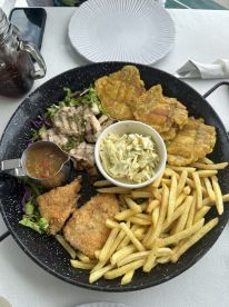 A beautifully arranged seafood platter featuring grilled fish, fried fish, tostones, coleslaw, and fries, perfect for enjoying after a fishing trip.