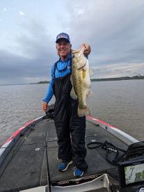 Angler proudly displaying a large Largemouth Bass while fishing from a bass boat on a calm lake.