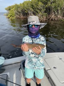 A young angler proudly displaying a caught fish while fishing in a mangrove area, showcasing the excitement of a successful outing.