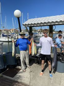 Two anglers proudly displaying their catch of Mahi Mahi and a large fish at a marina after a successful fishing trip.