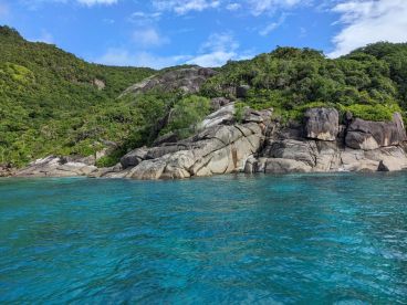 A scenic view of rocky cliffs and lush greenery along a vibrant blue coastline, ideal for fishing adventures.