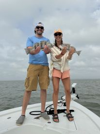 Two anglers proudly displaying their catch of Black Drum while standing on the bow of a fishing boat in a coastal waterway.