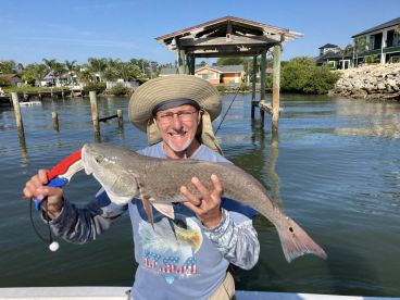 An enthusiastic angler proudly displaying a large Redfish caught in a scenic waterfront setting, showcasing a vibrant fishing environment.