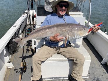 An angler proudly displaying a large Redfish while seated on a fishing boat, showcasing a successful day on the water.
