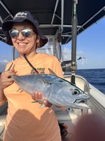 Angler smiling while holding a large fish on a boat during a deep-sea fishing trip.