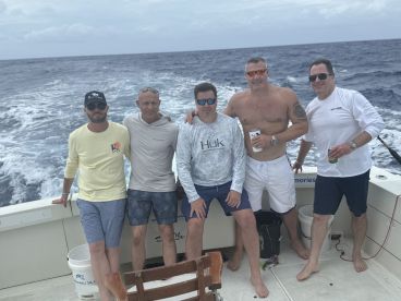 Group of five anglers enjoying a day on a sportfishing boat, with the ocean in the background.