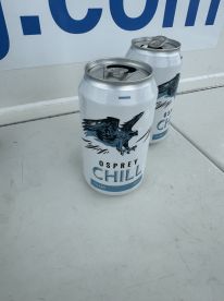 A close-up of two cans of Osprey Chill beer on a surface, with a sign partially visible in the background.