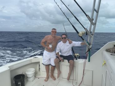 Two anglers enjoying a relaxed moment on the deck of a fishing boat, surrounded by ocean views, showcasing a casual fishing experience.