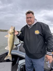 An angler proudly displaying a Walleye while fishing from a boat, showcasing a successful catch on a cloudy day.
