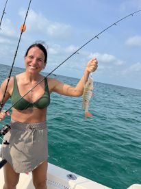 An angler proudly displaying a caught fish while fishing on a boat in clear blue waters.