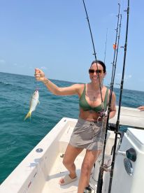 An angler proudly displaying a small Yellowtail Snapper while fishing from a boat in clear blue waters.