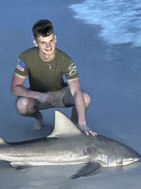 A young angler proudly displaying a large shark on the beach, showcasing a successful catch during a fishing trip.
