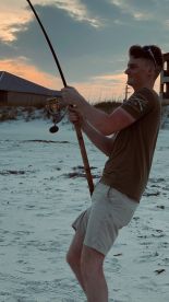 A young angler is actively reeling in a catch on the beach during sunset, showcasing the excitement of fishing in a coastal environment.