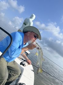 An angler proudly kisses a large Snook while fishing from a boat in calm waters, showcasing a successful catch during a day on the water.