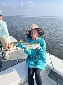 A young angler proudly displaying a Snook while fishing on a boat in a calm coastal environment.