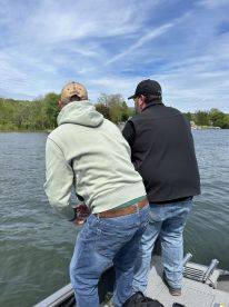 Two anglers actively fishing from a boat on a serene lake, showcasing a typical day of freshwater fishing.