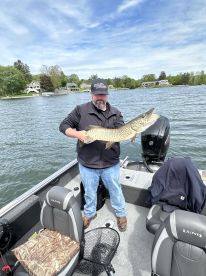 Angler proudly displaying a large Northern Pike while fishing from a Lund boat on a scenic lake.