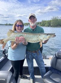 Two anglers proudly displaying a large Northern Pike while fishing on a scenic lake.