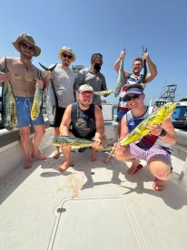 A group of six anglers proudly displaying their catch of Mahi Mahi and other species aboard a fishing boat, enjoying a sunny day on the water.