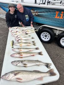 A young angler and an adult proudly display a variety of freshly caught fish, including several Walleye, arranged neatly on a table beside a fishing boat.