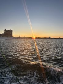 A scenic sunset view over the water, with a fishing rod visible in the foreground, capturing the tranquil atmosphere of a fishing trip.