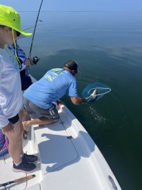 A young angler watches as an adult uses a net to catch a fish while fishing on a calm day in the open water.
