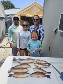 A family proudly displays their catch of several Largemouth Bass on a cleaning table after a successful fishing trip.