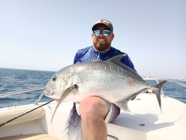Angler proudly displaying a large Giant Trevally while fishing on a boat in open waters.