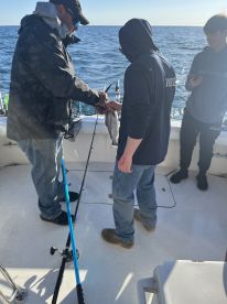 Two anglers actively engaged in fishing on a boat, with one holding a fish while the other assists. The scene captures the excitement of a fishing trip.