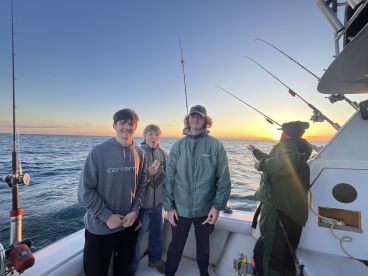 A group of young anglers enjoying a fishing trip at sunset, with rods in hand and a beautiful ocean backdrop.