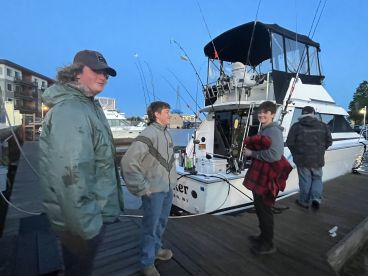 A group of young anglers preparing for a fishing trip by the boat, showcasing the exterior of a charter vessel at dusk.