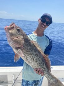 Angler proudly displaying a large Grouper while fishing offshore, showcasing a sunny day on the water.