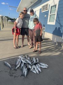 A family proudly displaying their catch of the day, featuring a variety of fish, at the dock after a successful fishing trip.
