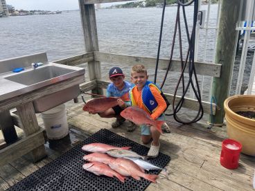 Two young anglers proudly displaying their catch of Red Snapper on a dock after a successful fishing trip.