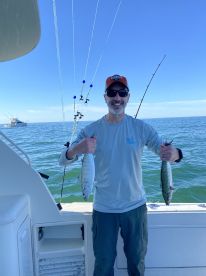 Angler proudly displaying two caught fish while aboard a sport fishing boat in open waters.