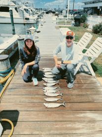 Two anglers posing with a neatly arranged catch of fish on the dock, showcasing their successful fishing trip.