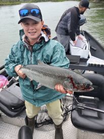 Young angler proudly holding a large salmon while fishing on a river, showcasing a successful catch during a guided trip.