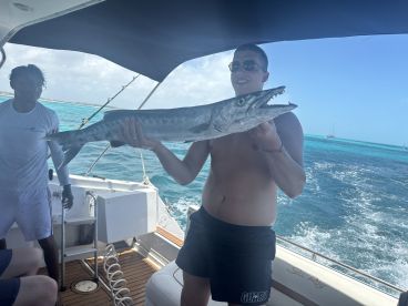 An angler proudly displaying a large Barracuda aboard a Sea Ray boat while enjoying a fishing trip in clear blue waters.