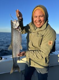 Angler proudly displaying a large Lake Trout while fishing on a clear day.