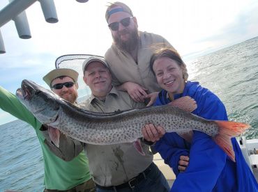 Group of anglers proudly displaying a large Northern Pike caught during a fishing trip on the water.