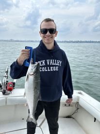 Angler proudly displaying a large Salmon while fishing from a boat, showcasing a successful catch on a cloudy day.