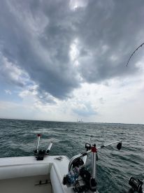 View from inside a fishing boat, showcasing the console and rod holders against a backdrop of cloudy skies and choppy waters.