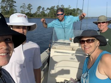 A cheerful group of anglers enjoying a day on the water, posing inside the boat with fishing gear visible.