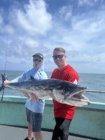 Two anglers proudly displaying a large King Mackerel on a fishing charter in open waters.