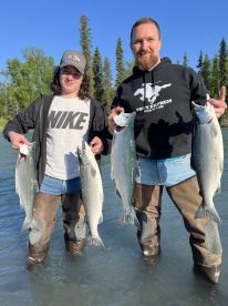 Two anglers proudly displaying their catch of silver salmon while standing in a river, showcasing a successful fishing trip.