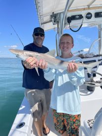 A young angler proudly displaying a caught shark while fishing on a boat, showcasing a sunny day on the water.
